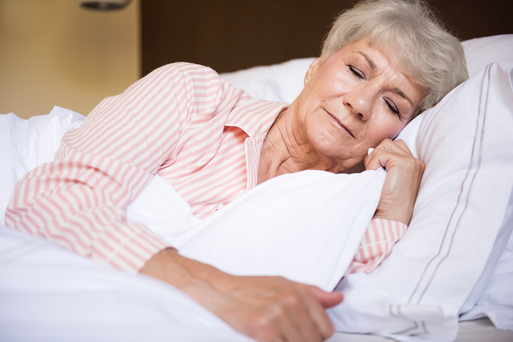 An elderly woman sleeping peacefully with a smile on her face.